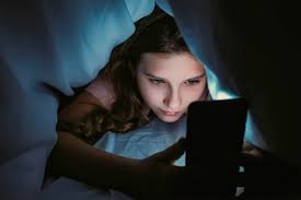 Adolescente qui regarde son téléphone dans le noir en dessous de ses couvertes.