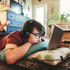 adolescent sur son lit en train de regarder son ordinateur avec des écouteurs