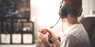 Un adolescent avec des écouteurs et une manette de console en train de jouer à un jeu vidéo.